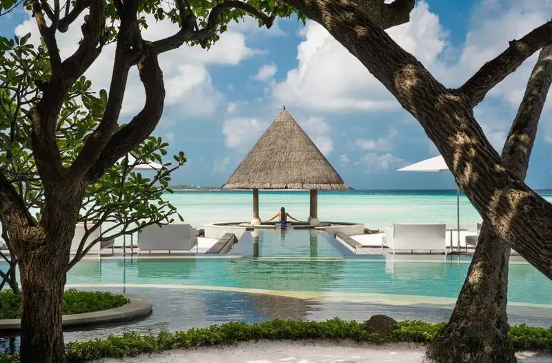 Une piscine turquoise bordée de chaises longues et d'une structure à toit de chaume.