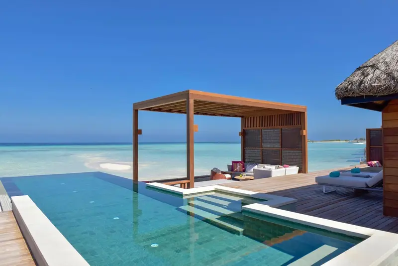 Terrasse en bois avec piscine et vue sur lagon turquoise.