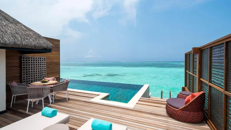 Terrasse en bois avec mobilier d'extérieur et piscine à débordement donnant sur une mer turquoise.