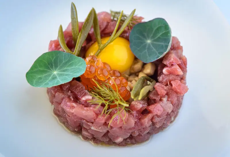 Assiette de viande crue, décorée d'une jaune d'œuf et d'herbes.