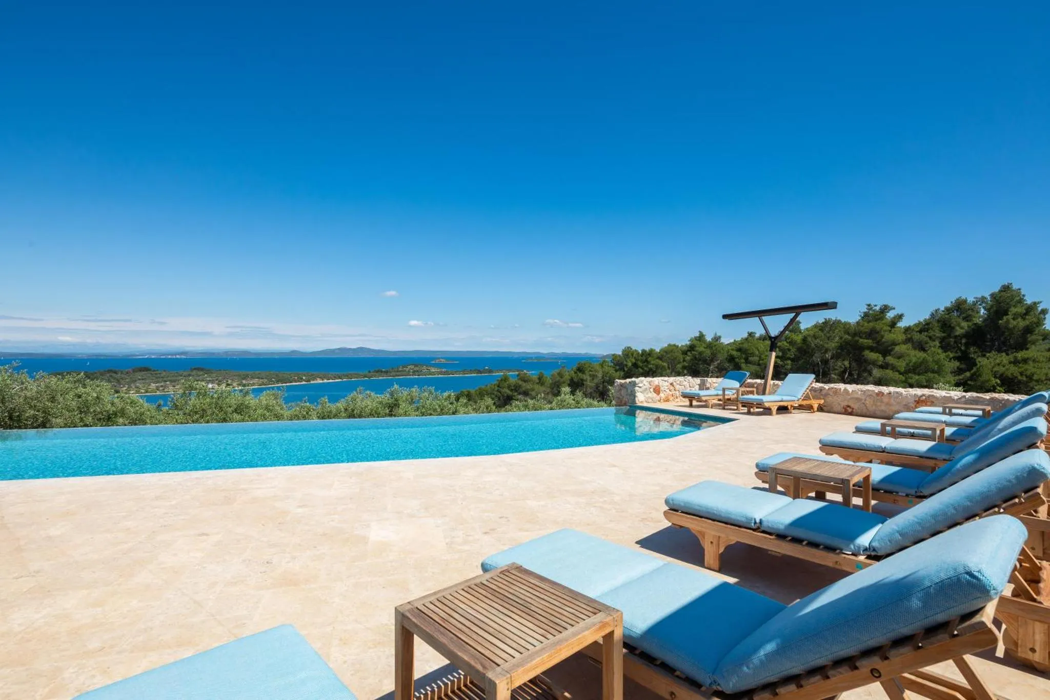 Terrasse avec transats et piscine à débordement offrant une vue sur la mer.