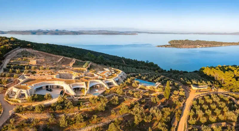 Vue aérienne d'un complexe hôtelier intégré à un paysage verdoyant en bord de mer.