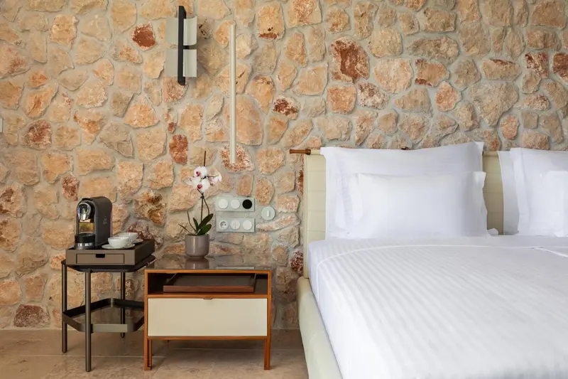 Une chambre lumineuse avec un lit blanc et un mur en pierre.