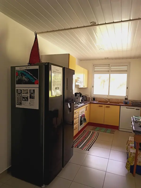 Une cuisine lumineuse avec un réfrigérateur noir et des meubles jaunes.