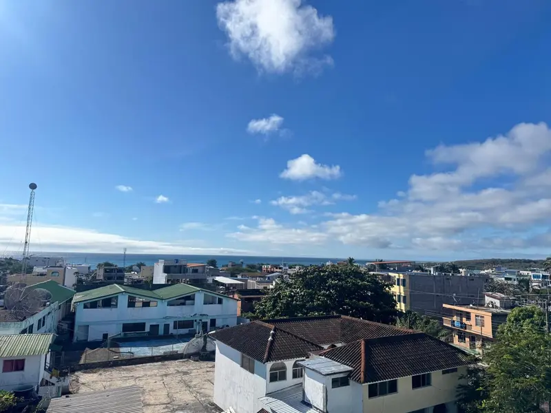 Vue aérienne sur une ville côtière ensoleillée avec des toits rouges et une mer bleue à l'horizon.