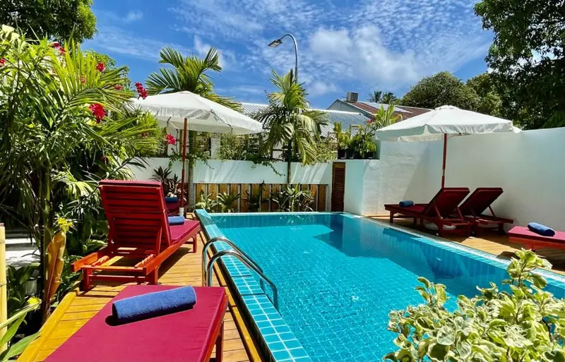 Transats rouges et parasols blancs bordent une piscine rectangulaire turquoise.