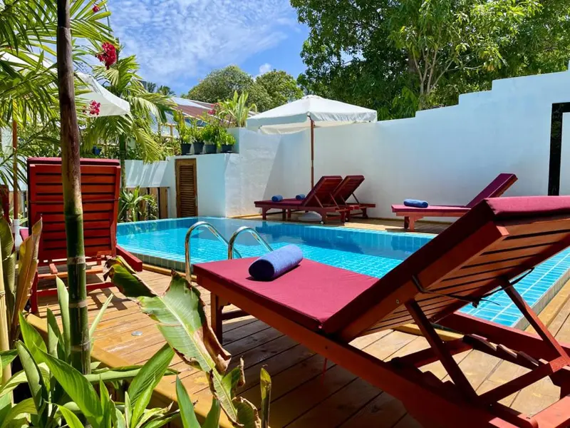Transats rouges bordant une piscine turquoise dans un jardin tropical.