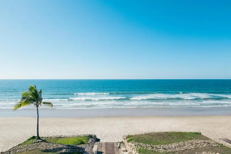 Plage de sable fin bordée d'une mer turquoise sous un ciel bleu dégagé.