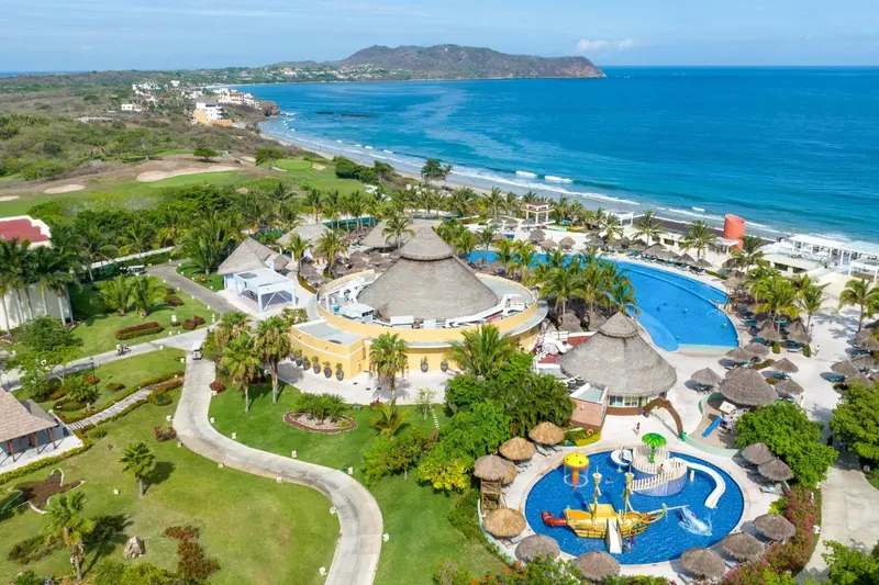 Vue aérienne d'un complexe hôtelier avec piscine et végétation luxuriante face à la mer.