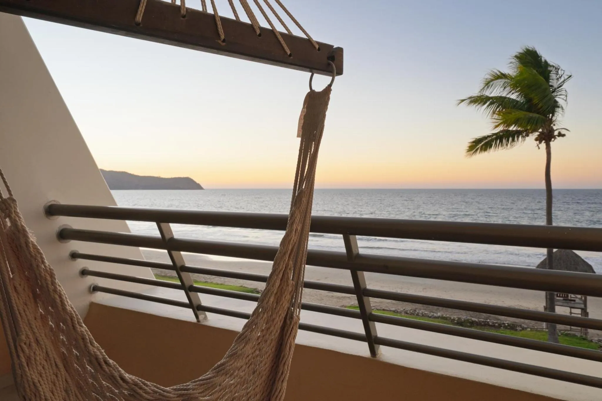 Un hamac suspendu sur une terrasse avec vue sur la mer au coucher du soleil.