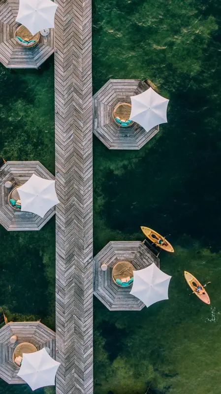 Terrasses en bois hexagonales surplombant une eau turquoise, avec parasols et transats.