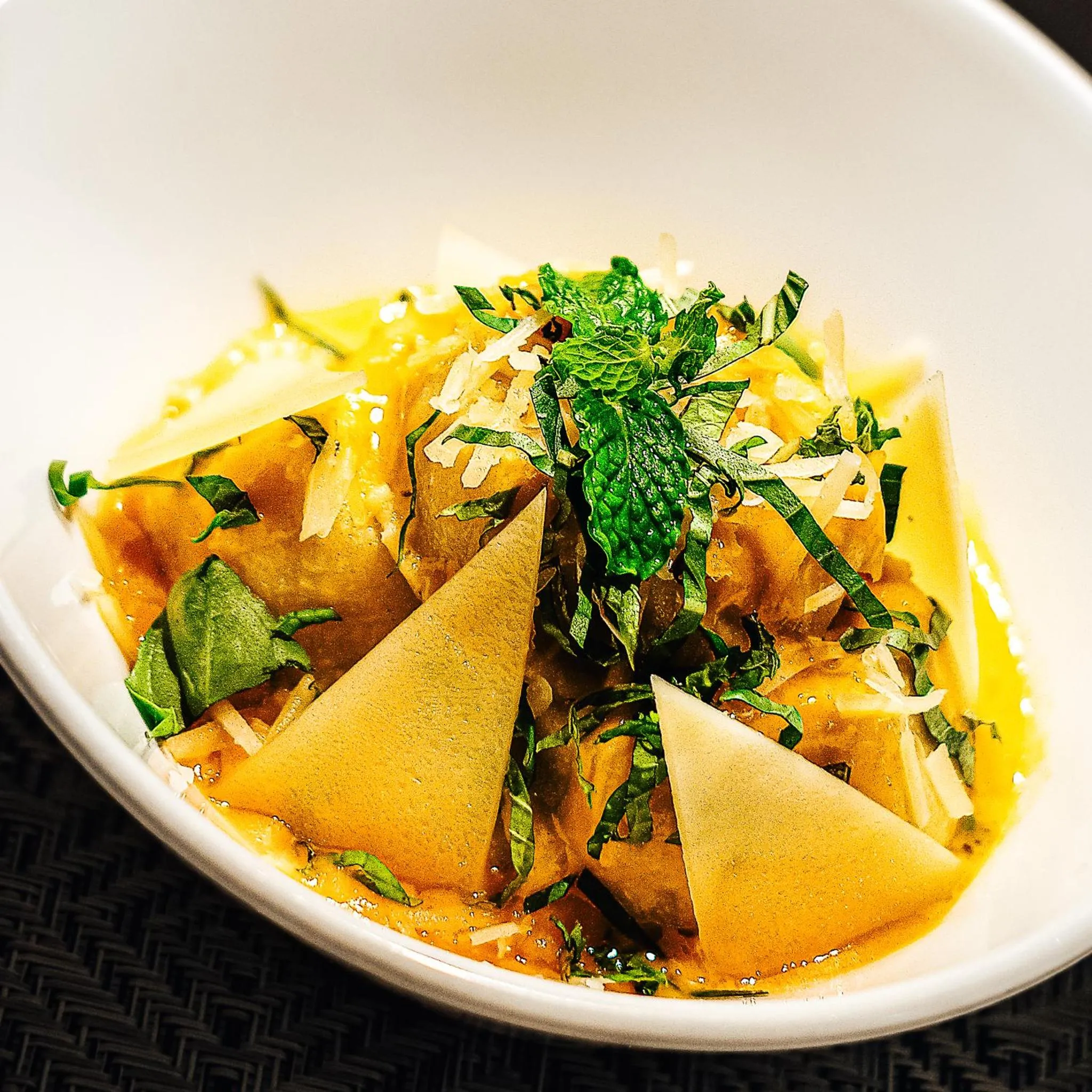 Un plat épicé servi dans un bol blanc est garni de verdure et de morceaux de pain.