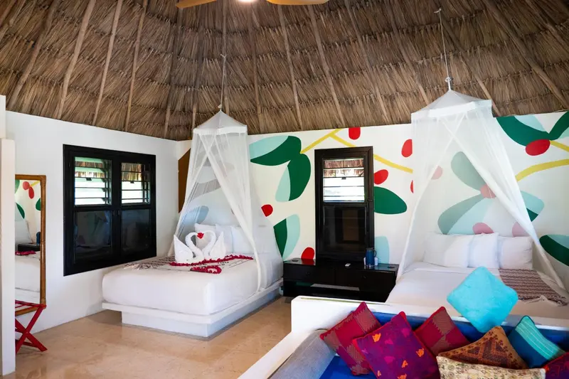 Chambre lumineuse avec deux lits décorés de moustiquaires et des murs colorés.