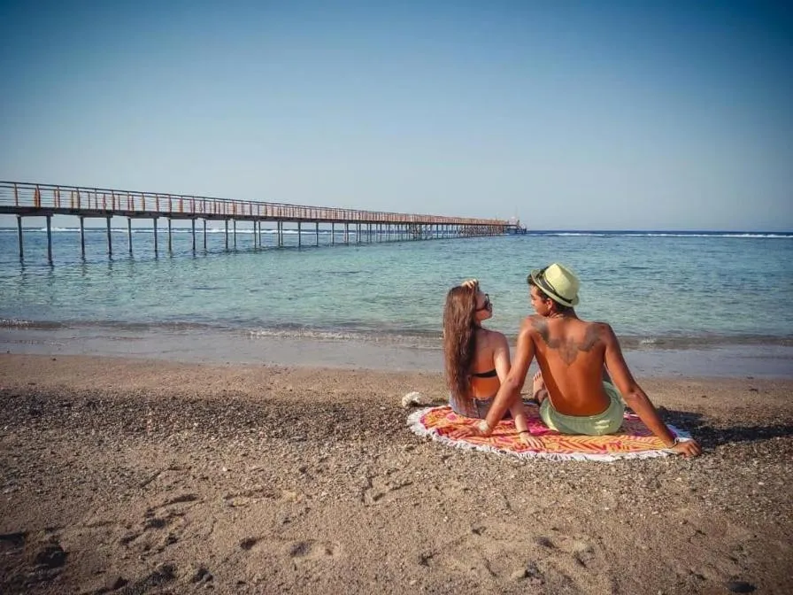 Deux personnes sont assises sur une plage de sable face à la mer.