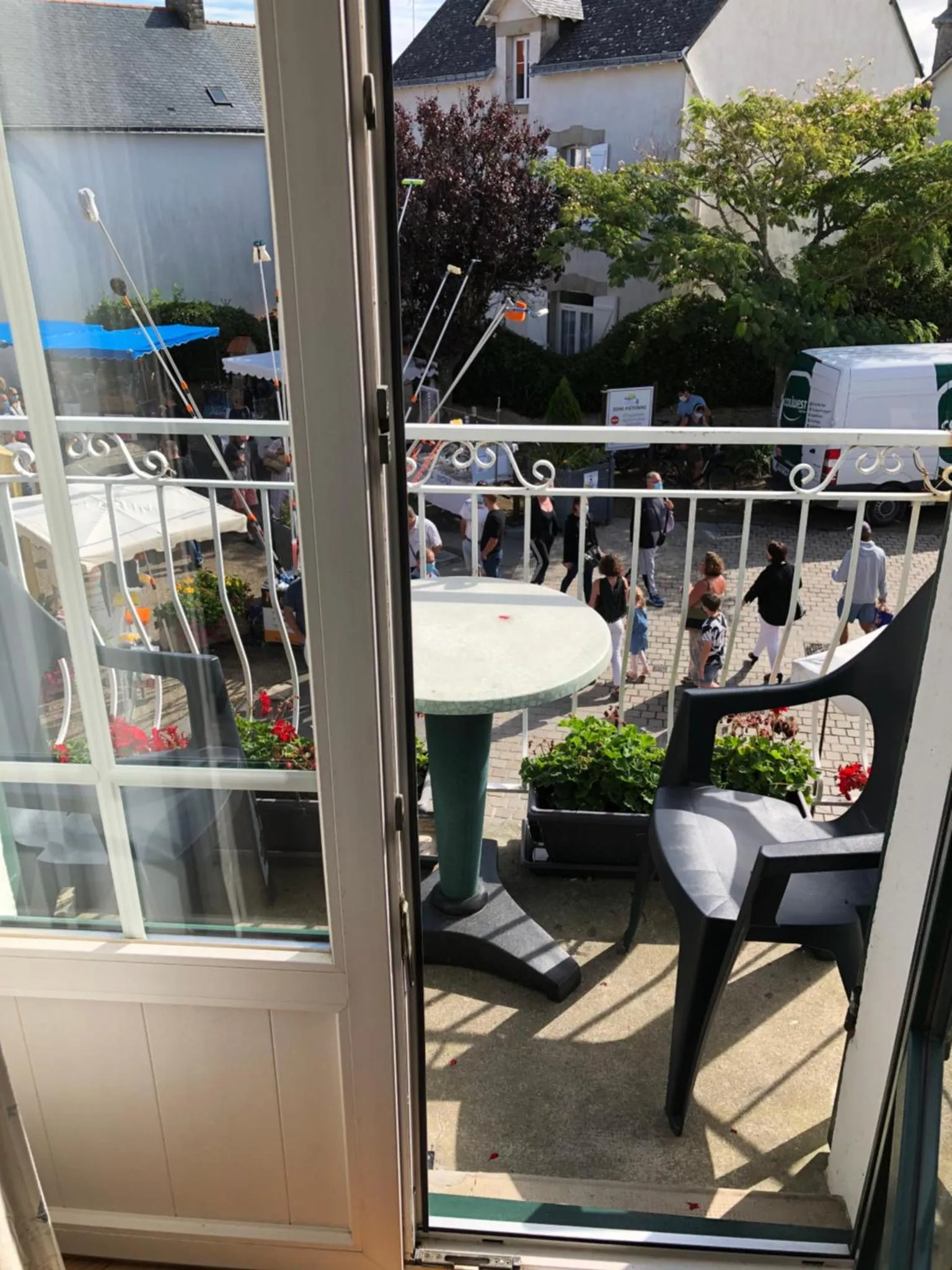 Une terrasse avec une table ronde et des chaises offre une vue sur une place animée.