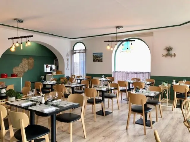 Une salle de restaurant lumineuse avec des tables dressées et une décoration sobre.