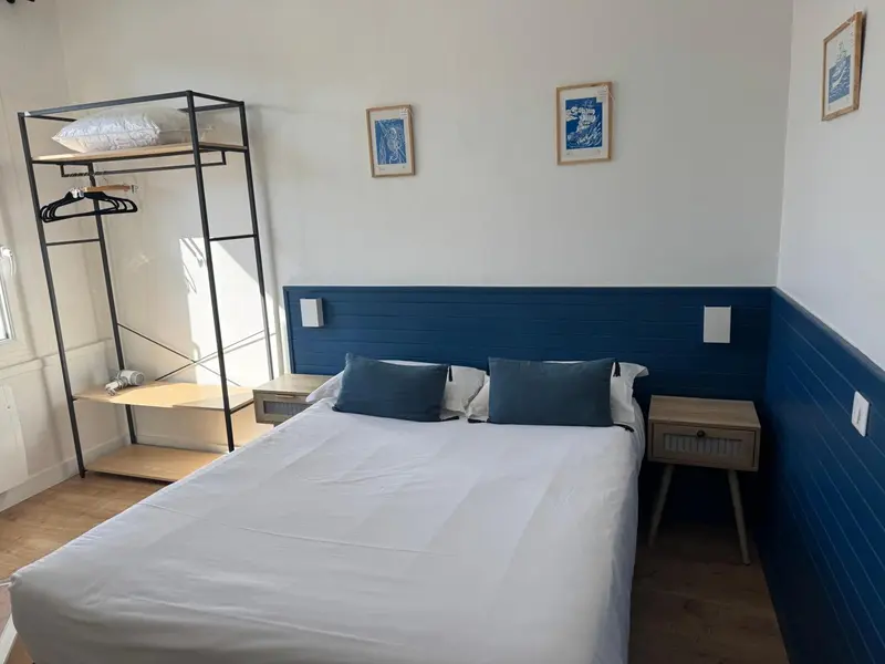Une chambre lumineuse avec un lit recouvert d'une courtepointe blanche et un portant à vêtements.