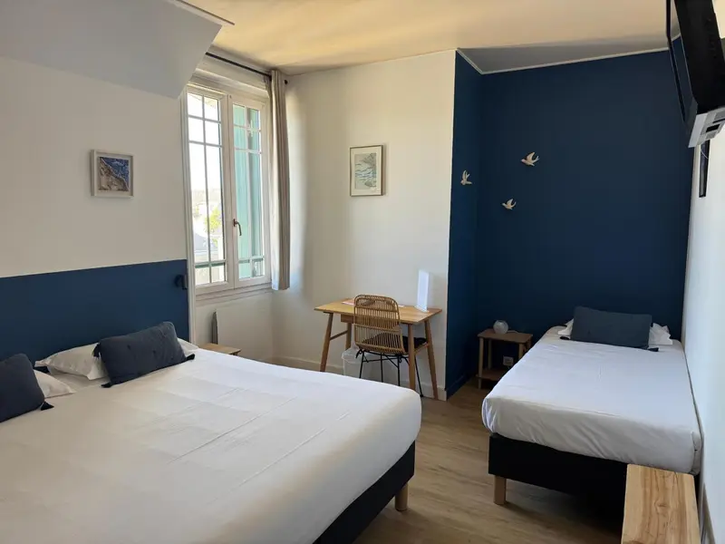 Une chambre lumineuse avec deux lits et un bureau près de la fenêtre.