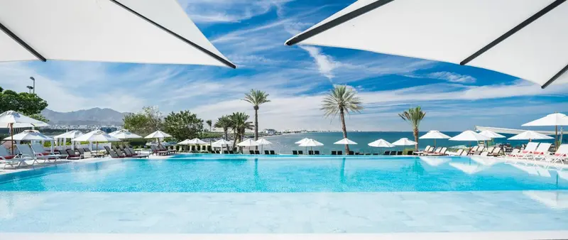 Vue sur une piscine à débordement avec des transats et des parasols blancs.
