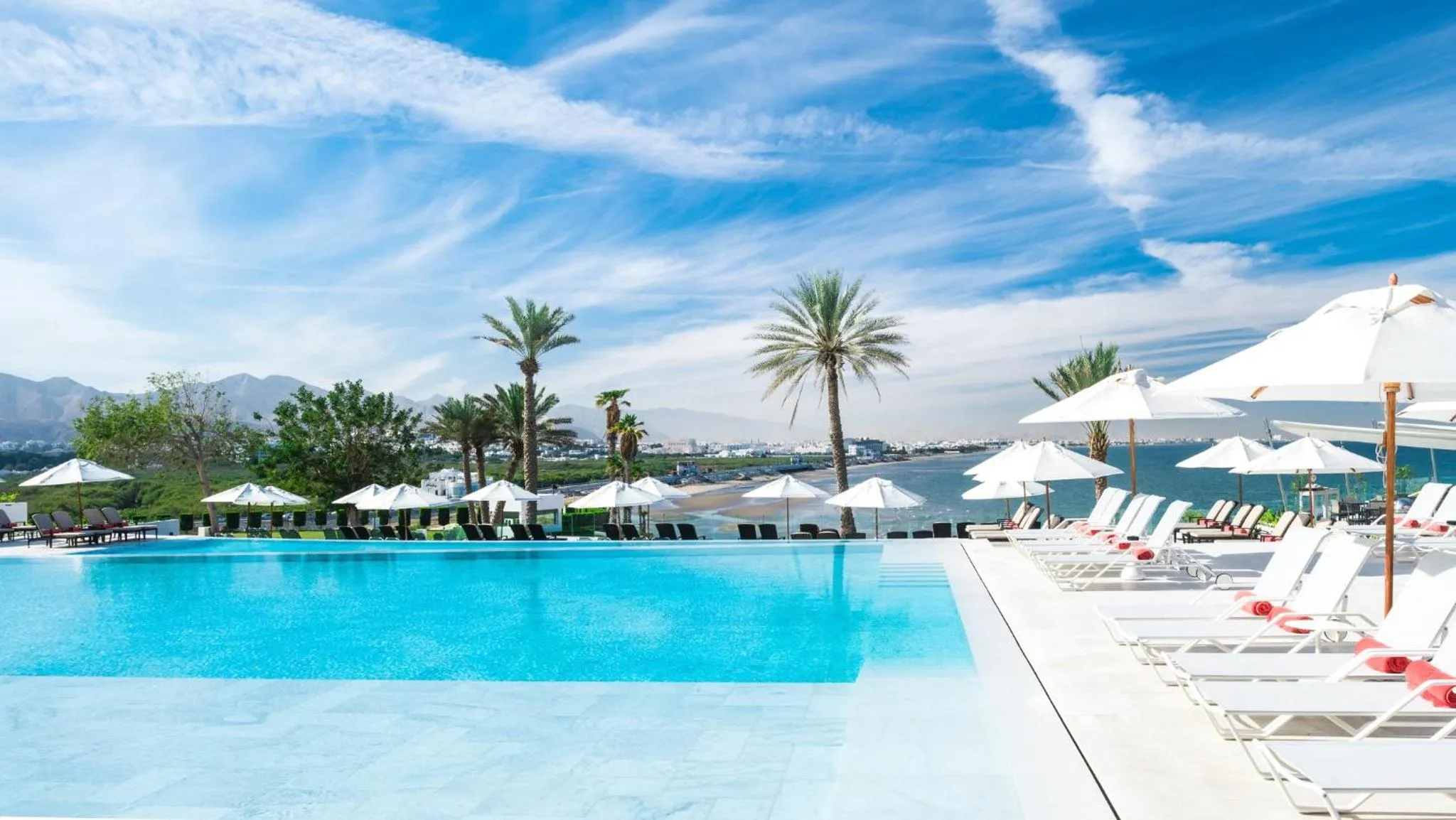 Transats blancs alignés au bord d'une piscine turquoise avec vue sur la mer.