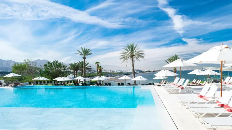 Transats blancs alignés au bord d'une piscine turquoise avec vue sur la mer.