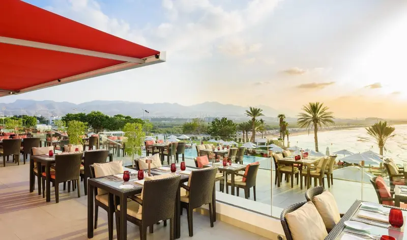 Une terrasse de restaurant offre une vue sur la mer et les montagnes au coucher du soleil.