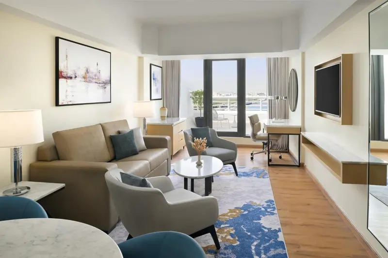 Un salon clair avec canapé, fauteuils et bureau près d'une grande fenêtre.
