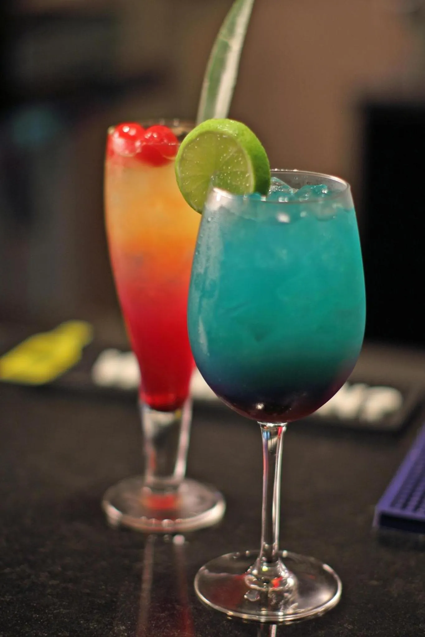 Deux cocktails colorés sont présentés sur un comptoir sombre.
