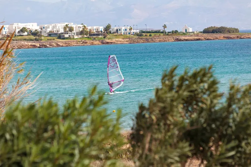 Une personne pratique la planche à voile sur une eau turquoise ensoleillée.