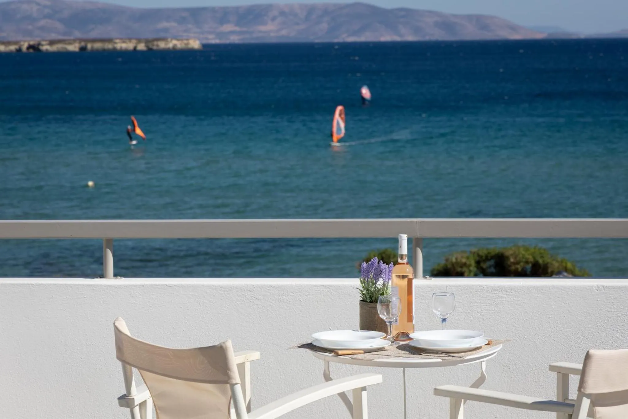 Une table avec des verres et une bouteille sur une terrasse ensoleillée avec vue sur la mer.