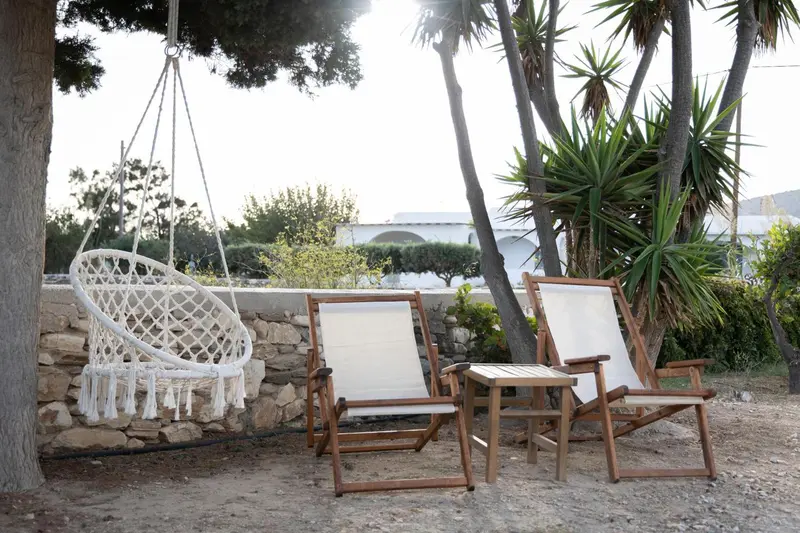 Deux transats et un fauteuil suspendu invitent à la détente dans un jardin ensoleillé.