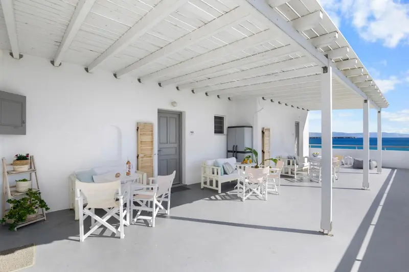 Terrasse ombragée avec mobilier blanc et vue sur la mer.