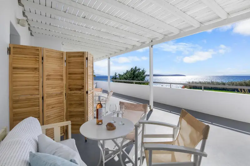 Terrasse ombragée avec table ronde et chaises, vue sur la mer.