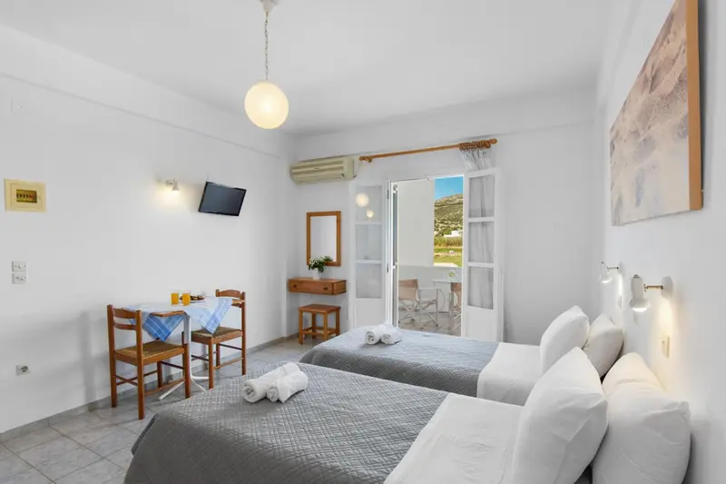 Une chambre lumineuse avec un lit double et un coin repas près d'une porte-fenêtre.