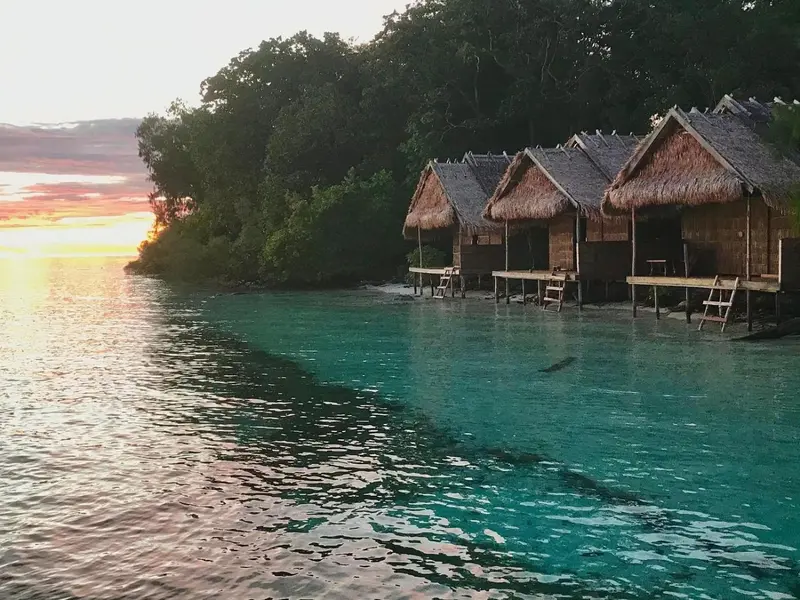 Cabanes sur pilotis au bord d'une mer turquoise au coucher du soleil.