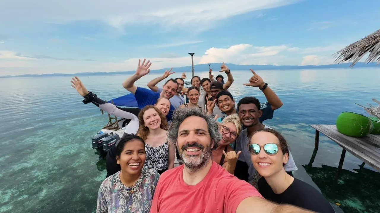 Groupe de personnes souriantes posant sur un ponton en bois face à la mer.