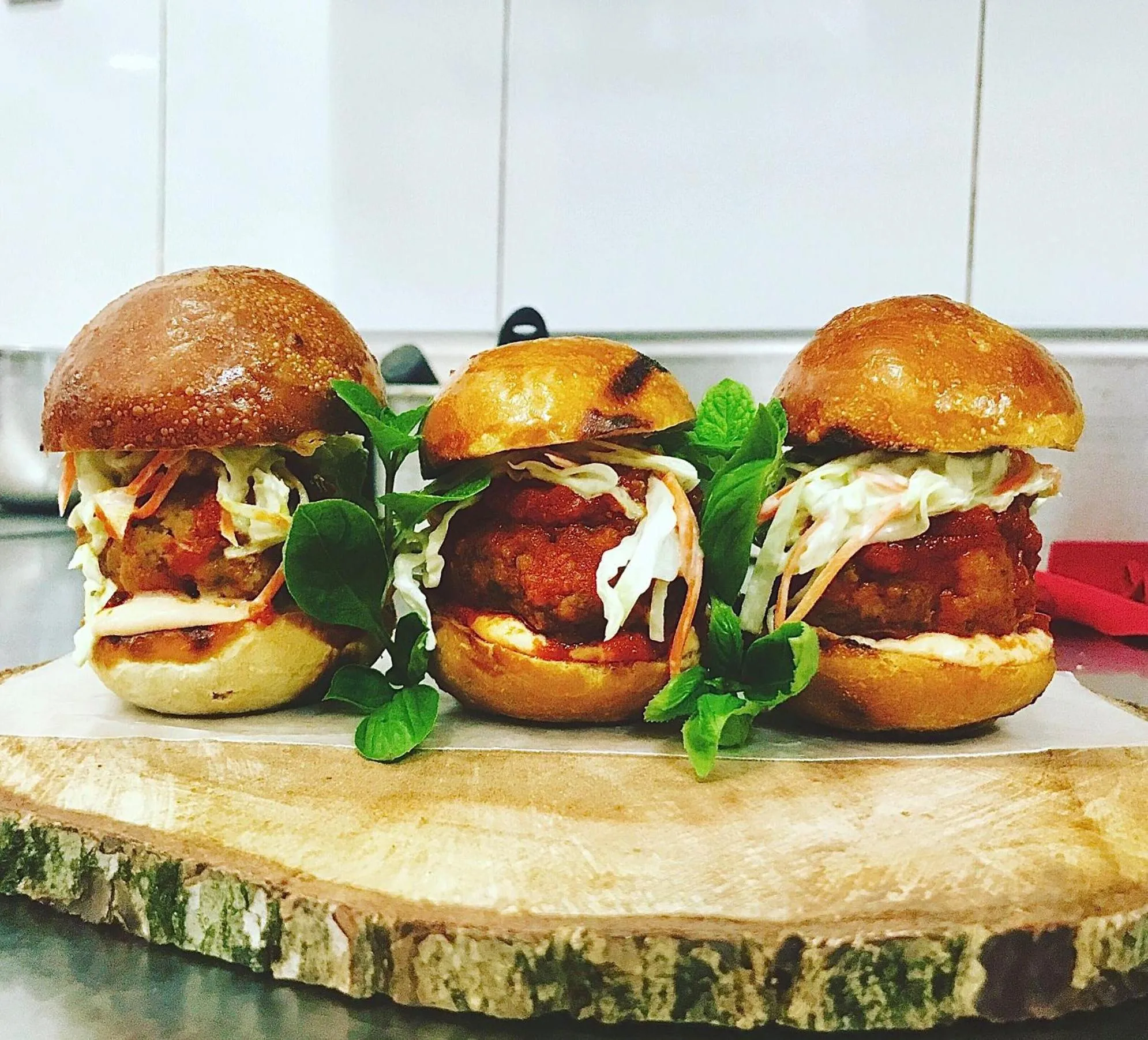 Trois mini-burgers garnis de salade et de sauce sont présentés sur une planche en bois.
