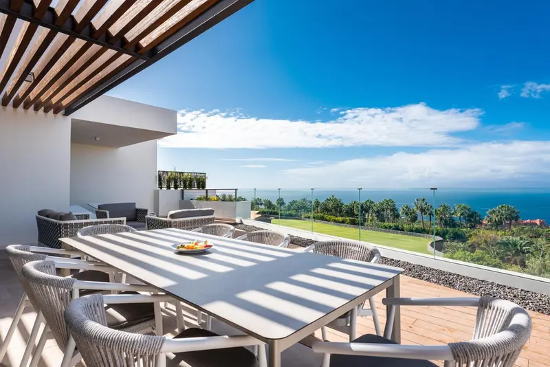 Une table à manger est mise en scène sur une terrasse ensoleillée avec vue sur la mer.
