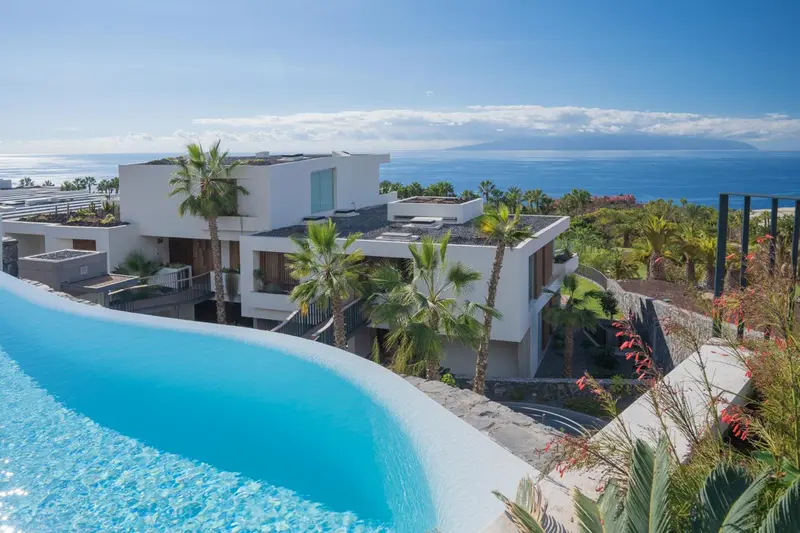Vue aérienne d'un complexe hôtelier moderne avec piscine et végétation luxuriante face à la mer.