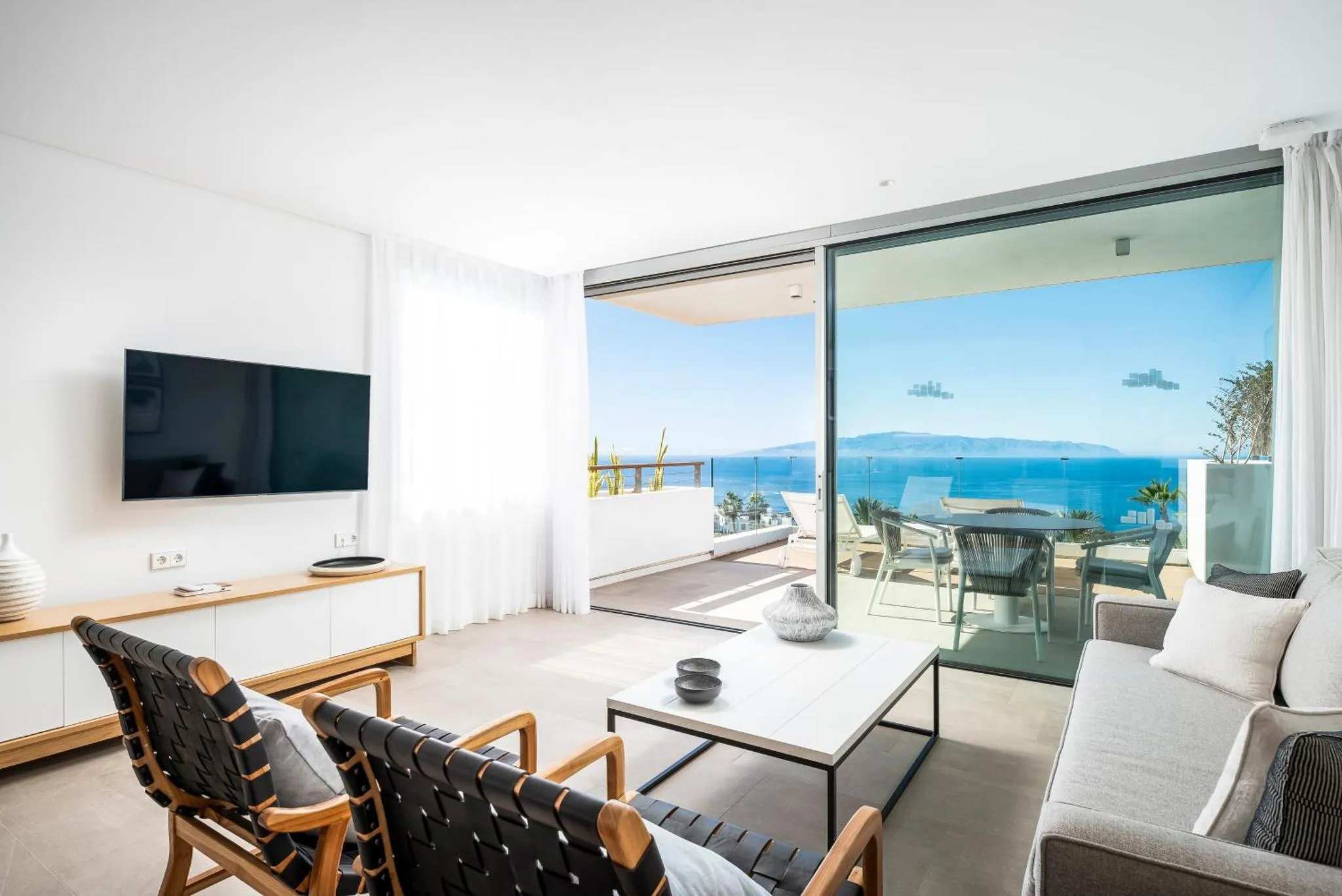 Espace de détente lumineux avec canapés et vue sur la mer depuis une terrasse.