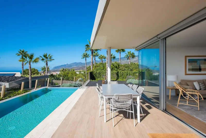 Terrasse avec table à manger et piscine à débordement donnant sur un paysage montagneux.