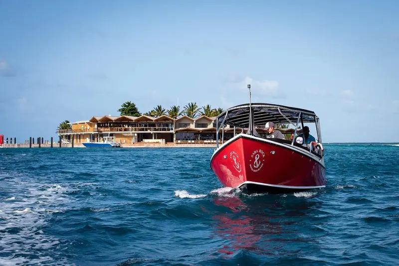 Un bateau rouge navigue sur une mer bleue en direction d'une structure côtière.