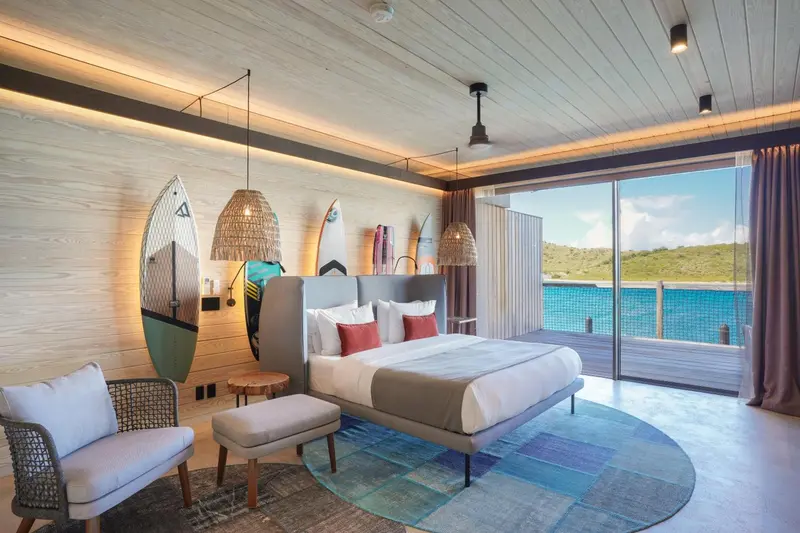Une chambre lumineuse avec un grand lit et un fauteuil près d'une fenêtre donnant sur la mer.