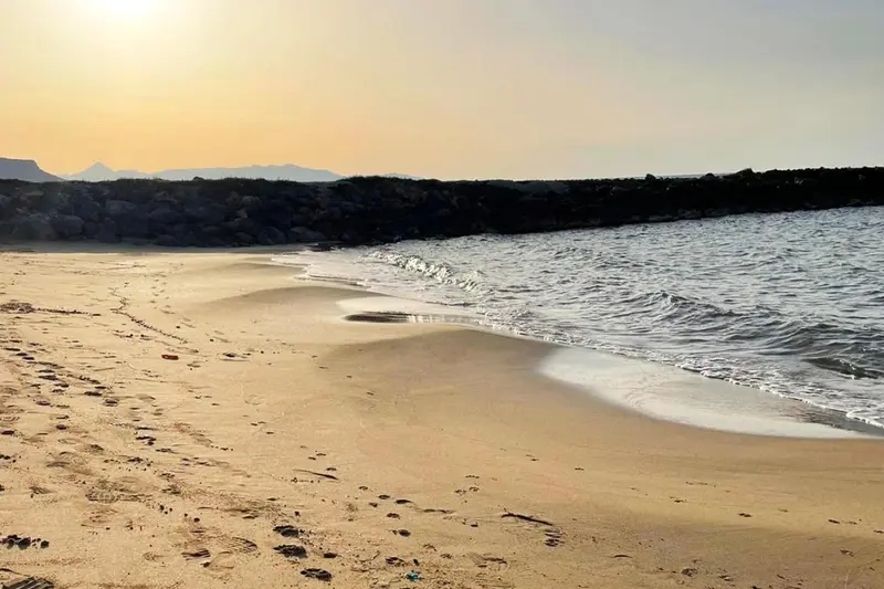 Plage de sable fin bordée par une mer calme au coucher du soleil.