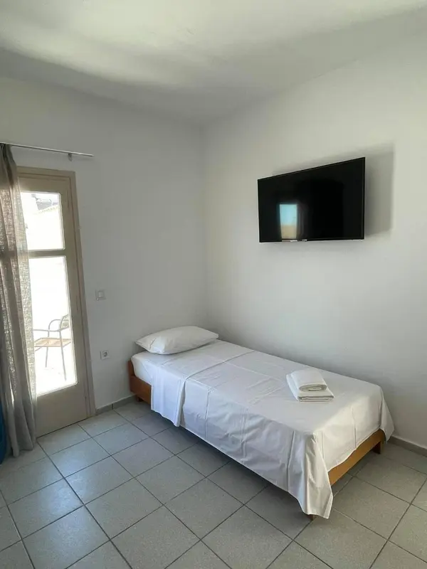 Une chambre lumineuse avec un lit simple et une télévision murale.