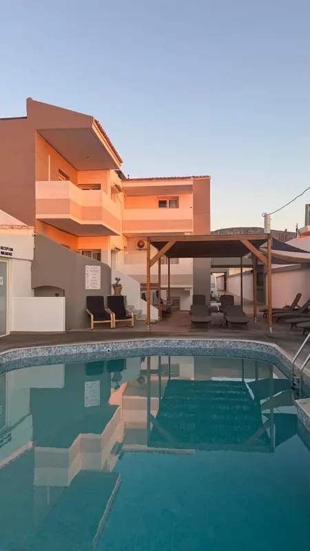 Bâtiment blanc et bleu avec piscine au premier plan et ciel orangé au loin.
