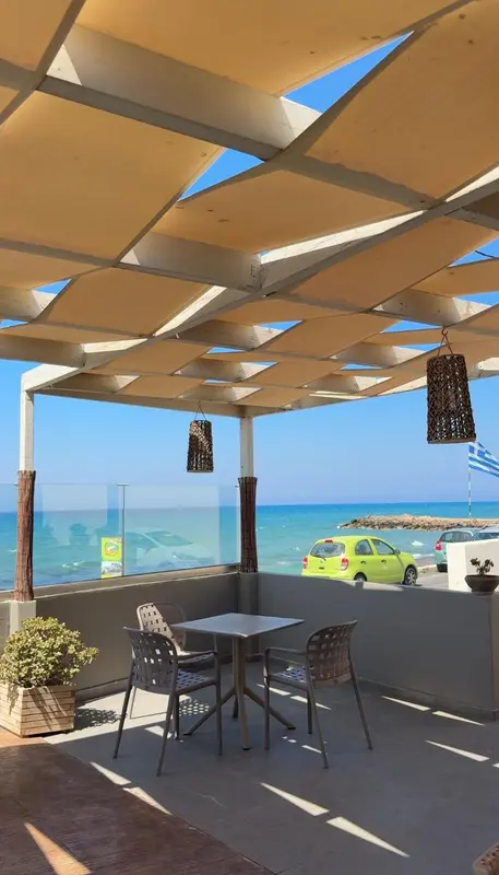Terrasse ombragée avec mobilier de jardin et vue sur la mer.