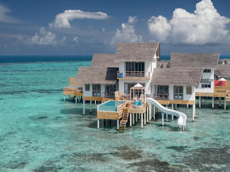 Maisons sur pilotis avec piscine et toboggan au-dessus d'un lagon turquoise.