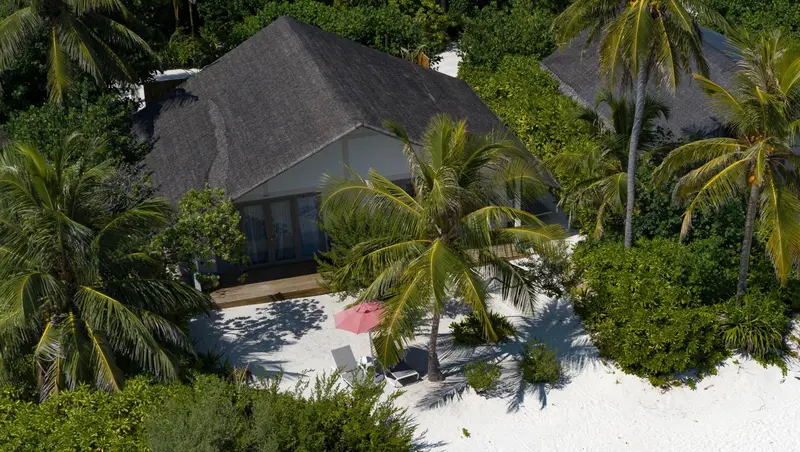 Vue aérienne de bungalows sur une plage de sable blanc bordée de palmiers.