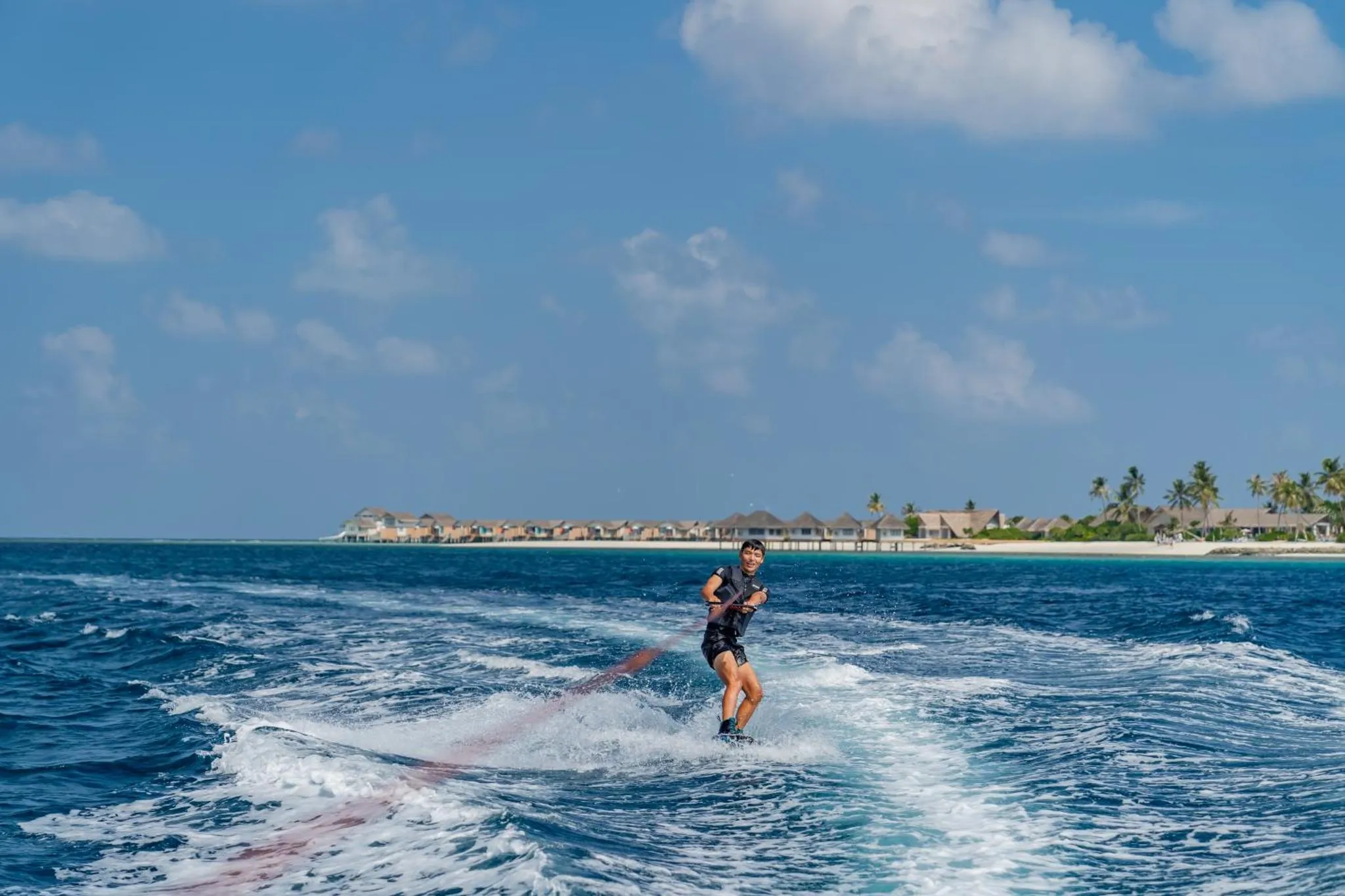 Une personne pratique le kitesurf sur une eau turquoise face à des bungalows sur pilotis.